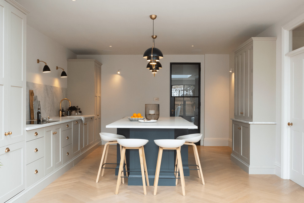 Inspiration for a large traditional single-wall kitchen/diner in London with grey cabinets, an island, white worktops, shaker cabinets, integrated appliances, light hardwood flooring and beige floors.