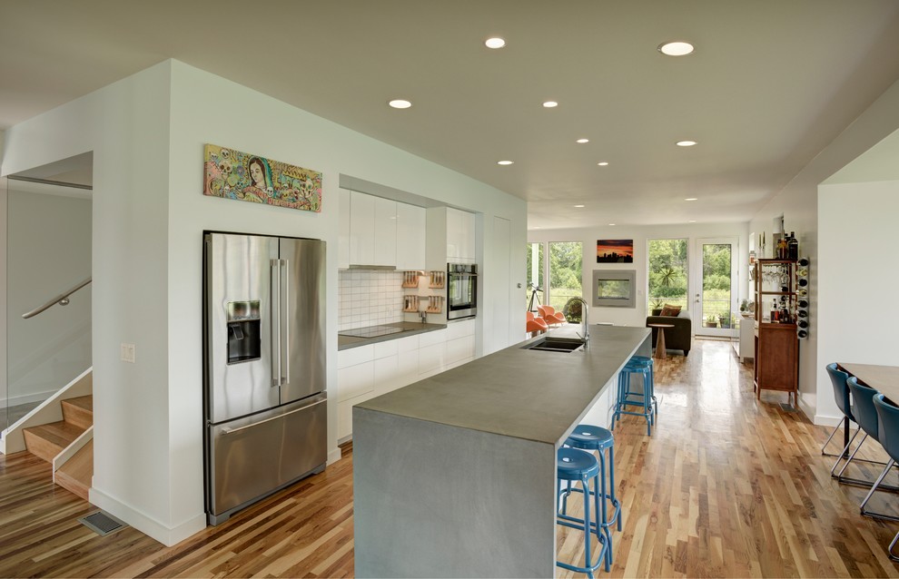 Exempel på ett modernt kök med öppen planlösning, med en dubbel diskho, släta luckor, vita skåp, bänkskiva i betong, vitt stänkskydd, rostfria vitvaror, mellanmörkt trägolv och en köksö