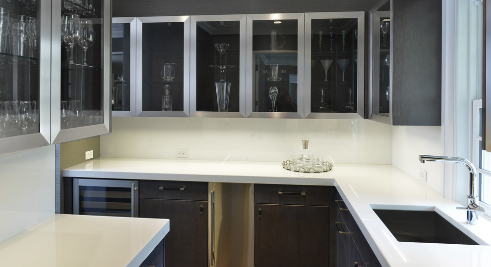 Cette image montre une grande cuisine minimaliste en L et inox fermée avec un évier encastré, un placard à porte vitrée, un plan de travail en quartz modifié, une crédence blanche et aucun îlot.