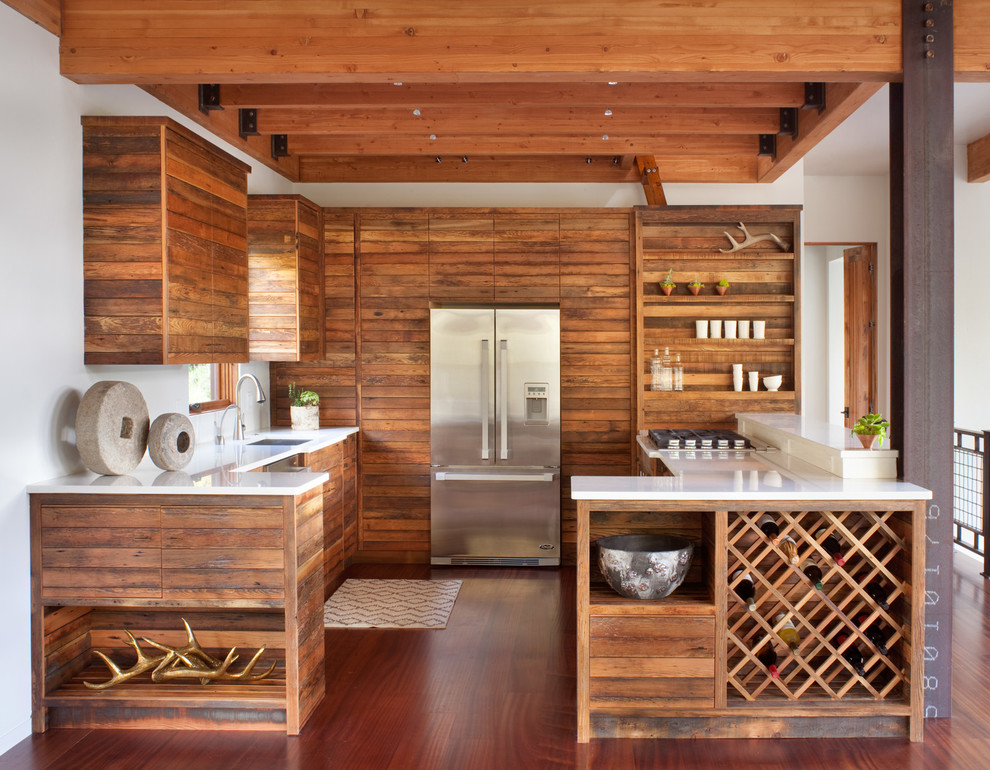 Exemple d'une cuisine montagne en bois brun et U avec plan de travail en marbre, un électroménager en acier inoxydable, un sol en bois brun, une péninsule, un évier encastré et un placard sans porte.