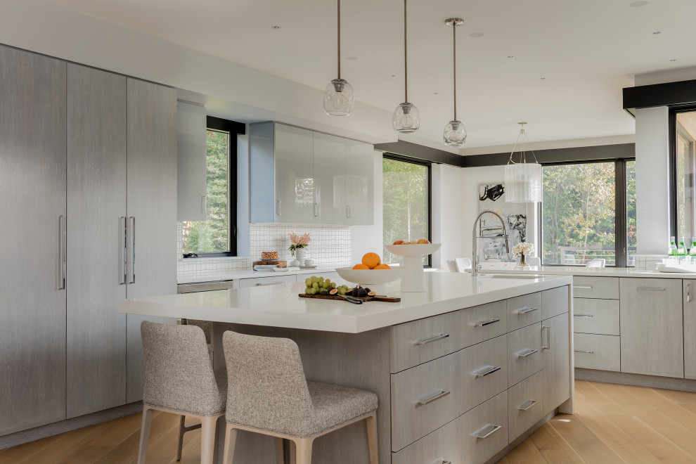 Contemporary kitchen pantry in Boston with a built-in sink, flat-panel cabinets, white splashback, ceramic splashback, stainless steel appliances, light hardwood flooring, an island and white worktops.