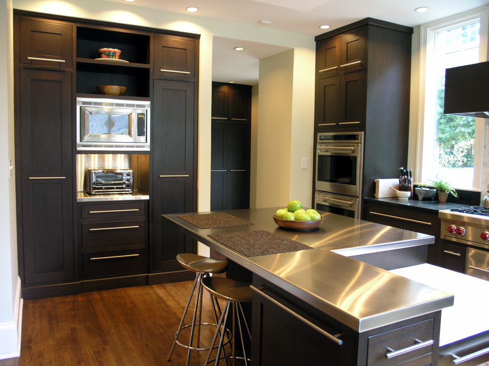Ejemplo de cocina contemporánea con encimera de acero inoxidable, electrodomésticos de acero inoxidable, puertas de armario de madera en tonos medios y armarios estilo shaker