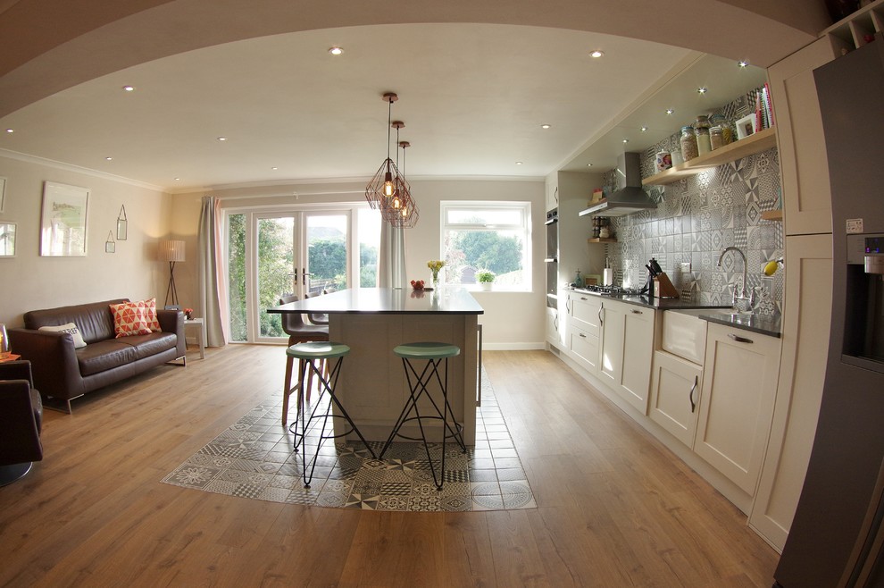 Photo of a large modern grey and white single-wall kitchen/diner in Cardiff with a belfast sink, shaker cabinets, white cabinets, quartz worktops, multi-coloured splashback, ceramic splashback, stainless steel appliances, laminate floors, an island, multi-coloured floors, black worktops and a feature wall.
