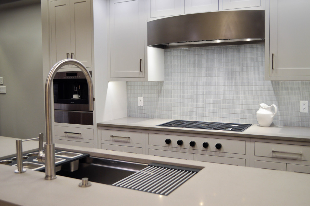 This is an example of a medium sized traditional galley kitchen in Cleveland with a submerged sink, shaker cabinets, white cabinets, engineered stone countertops, grey splashback, porcelain splashback, stainless steel appliances, medium hardwood flooring, an island, brown floors and white worktops.