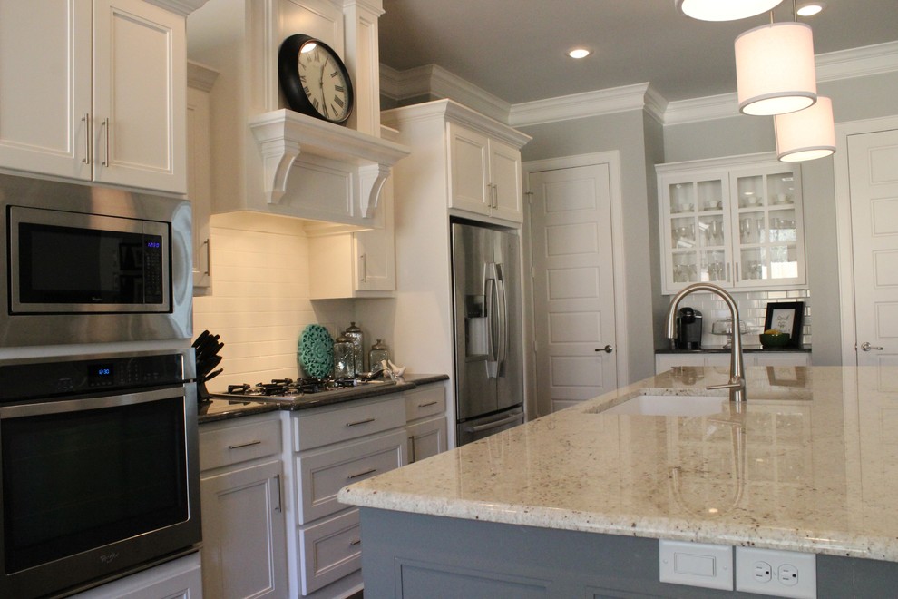 Inredning av ett klassiskt mellanstort kök, med en undermonterad diskho, luckor med glaspanel, vita skåp, granitbänkskiva, vitt stänkskydd, stänkskydd i tunnelbanekakel, rostfria vitvaror och en köksö