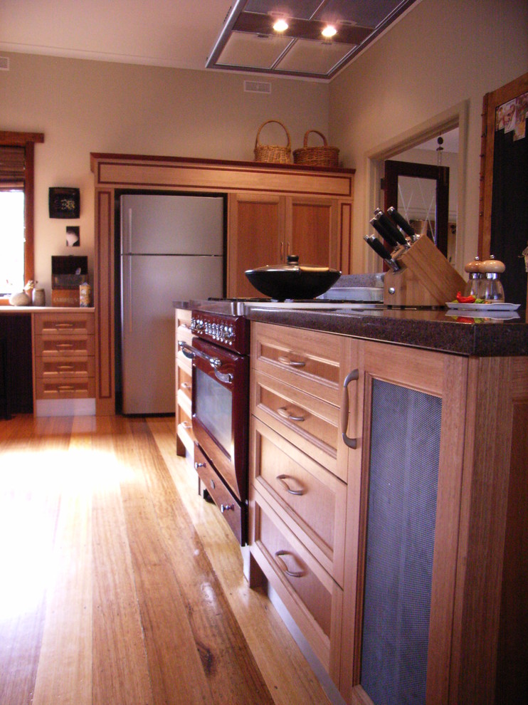 Inredning av ett modernt mellanstort kök, med en nedsänkt diskho, skåp i shakerstil, skåp i ljust trä, bänkskiva i kvarts, rött stänkskydd, glaspanel som stänkskydd, färgglada vitvaror, ljust trägolv och en köksö