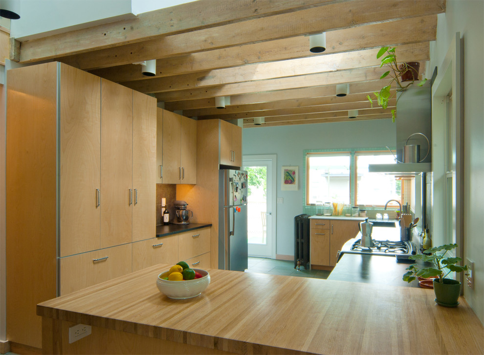 Bild på ett funkis kök, med en integrerad diskho, släta luckor, skåp i ljust trä, träbänkskiva, grönt stänkskydd, stänkskydd i stenkakel, rostfria vitvaror, skiffergolv och en halv köksö