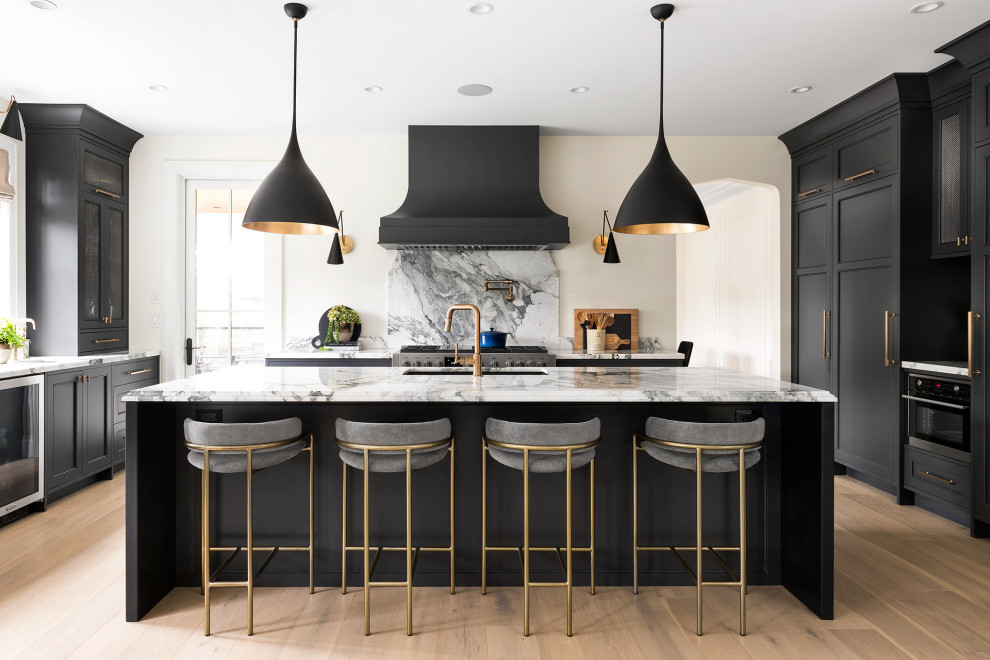 Large traditional u-shaped kitchen/diner in Vancouver with a submerged sink, recessed-panel cabinets, black cabinets, marble worktops, white splashback, granite splashback, black appliances, light hardwood flooring, an island, brown floors and white worktops.