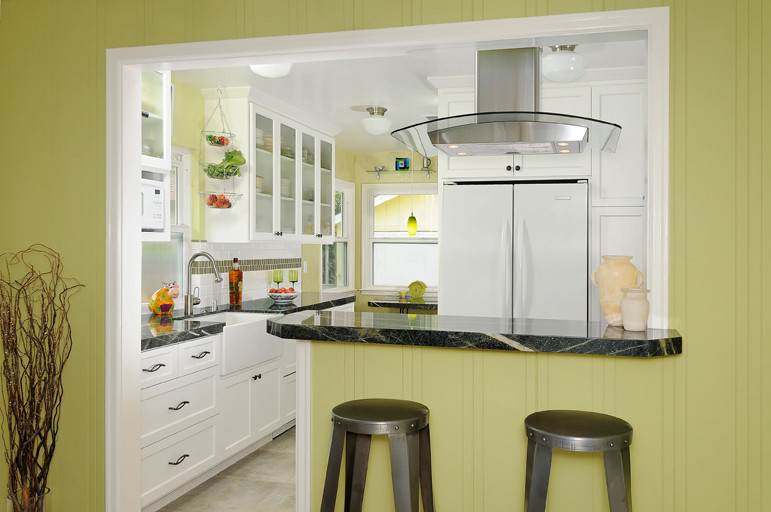 Foto på ett litet funkis kök, med en rustik diskho, luckor med infälld panel, vita skåp, granitbänkskiva, vitt stänkskydd, stänkskydd i tunnelbanekakel, vita vitvaror, klinkergolv i porslin och en halv köksö