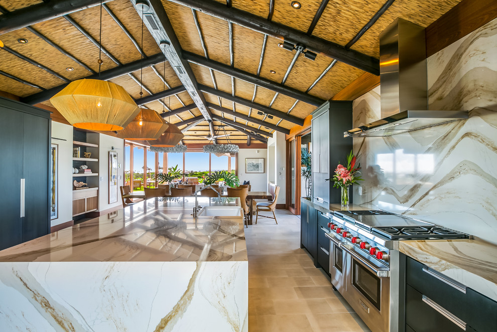 Photo of a large modern galley open plan kitchen in Hawaii with a belfast sink, flat-panel cabinets, black cabinets, engineered stone countertops, beige splashback, stainless steel appliances, ceramic flooring, an island, grey floors and brown worktops.