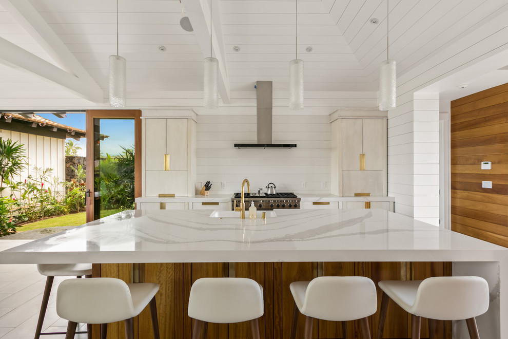 ハワイにある広いビーチスタイルのおしゃれなキッチン (エプロンフロントシンク、フラットパネル扉のキャビネット、白いキャビネット、クオーツストーンカウンター、白いキッチンパネル、石スラブのキッチンパネル、シルバーの調理設備、磁器タイルの床、グレーの床) の写真