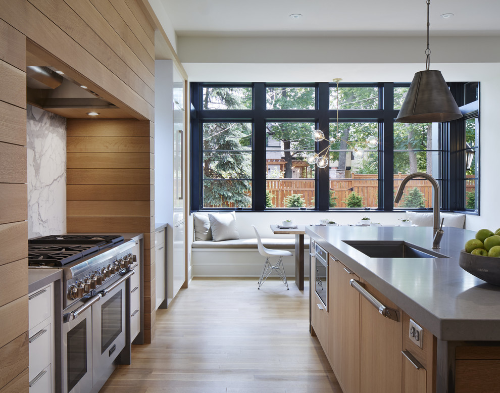Example of a transitional galley light wood floor eat-in kitchen design in Minneapolis with an undermount sink, flat-panel cabinets, white cabinets, solid surface countertops, white backsplash, stone slab backsplash, an island and stainless steel appliances