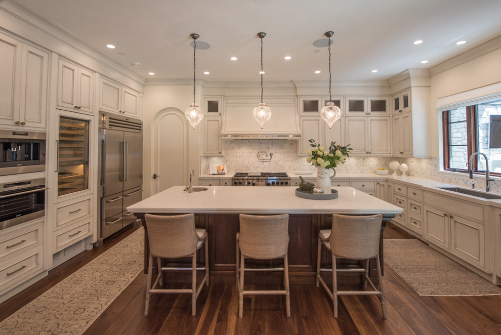 Example of a huge tuscan u-shaped medium tone wood floor eat-in kitchen design in Vancouver with an undermount sink, recessed-panel cabinets, distressed cabinets, limestone countertops, multicolored backsplash, ceramic backsplash, stainless steel appliances and an island