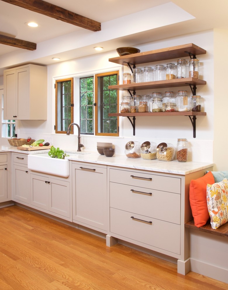 Inspiration for a mid-sized farmhouse galley medium tone wood floor open concept kitchen remodel in New York with a farmhouse sink, flat-panel cabinets, beige cabinets, marble countertops, white backsplash, subway tile backsplash, stainless steel appliances and a peninsula