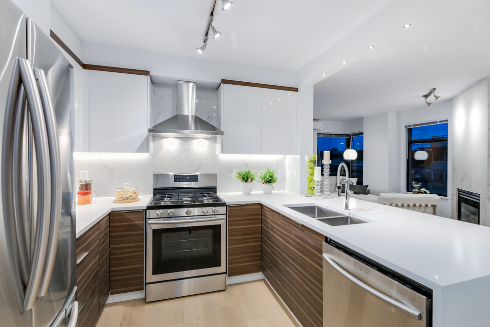 Design ideas for a medium sized contemporary u-shaped kitchen/diner in Vancouver with a submerged sink, flat-panel cabinets, white cabinets, engineered stone countertops, white splashback, porcelain splashback, stainless steel appliances, light hardwood flooring and a breakfast bar.