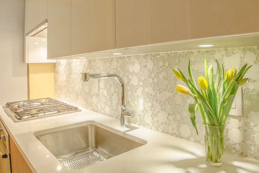 This is an example of a modern galley enclosed kitchen in New York with a submerged sink, flat-panel cabinets, medium wood cabinets, white splashback, glass tiled splashback and no island.