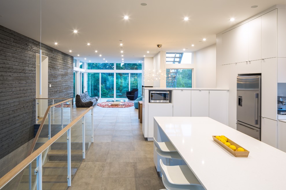 Large contemporary l-shaped open plan kitchen in Ottawa with flat-panel cabinets, white cabinets, stainless steel appliances, an island, a submerged sink, composite countertops, white splashback and concrete flooring.