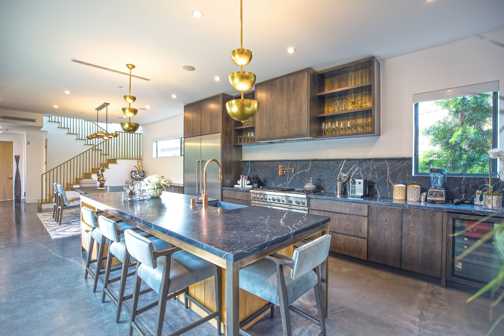 Contemporary galley open plan kitchen in Los Angeles with a belfast sink, flat-panel cabinets, dark wood cabinets, grey splashback, stainless steel appliances, concrete flooring, an island and grey floors.