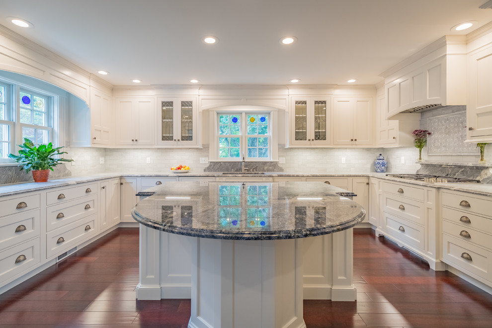 Exempel på ett stort klassiskt grå grått u-kök, med en undermonterad diskho, luckor med infälld panel, vita skåp, granitbänkskiva, grått stänkskydd, stänkskydd i keramik, rostfria vitvaror, mörkt trägolv, en köksö och brunt golv