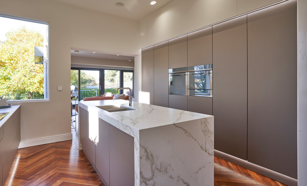 Inspiration for a large modern galley open plan kitchen in Other with a double-bowl sink, flat-panel cabinets, brown cabinets, engineered stone countertops, beige splashback, glass sheet splashback, stainless steel appliances, dark hardwood flooring, an island, brown floors and beige worktops.