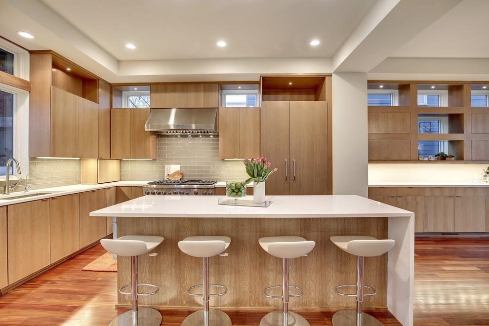 Inspiration for a mid-sized modern l-shaped medium tone wood floor open concept kitchen remodel in Minneapolis with a single-bowl sink, flat-panel cabinets, medium tone wood cabinets, solid surface countertops, gray backsplash, glass tile backsplash, paneled appliances and an island