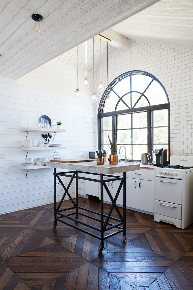 Ejemplo de cocina de estilo de casa de campo con salpicadero blanco, salpicadero de azulejos tipo metro, electrodomésticos blancos, suelo de madera oscura, una isla y armarios con paneles lisos