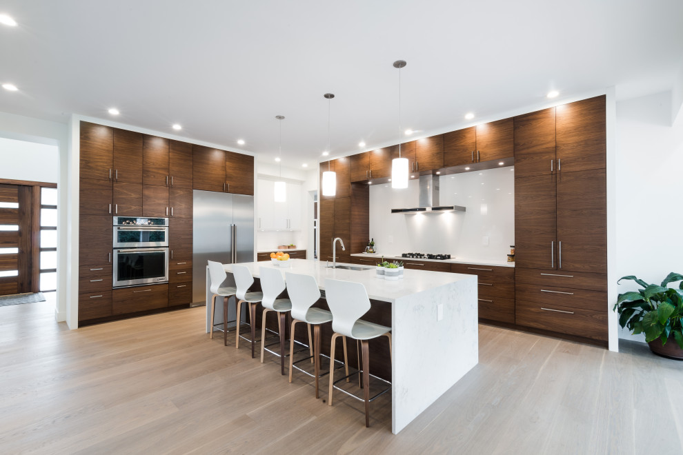 This is an example of a large contemporary l-shaped open plan kitchen in Detroit with a single-bowl sink, flat-panel cabinets, medium wood cabinets, engineered stone countertops, white splashback, porcelain splashback, stainless steel appliances, light hardwood flooring, an island, beige floors and white worktops.