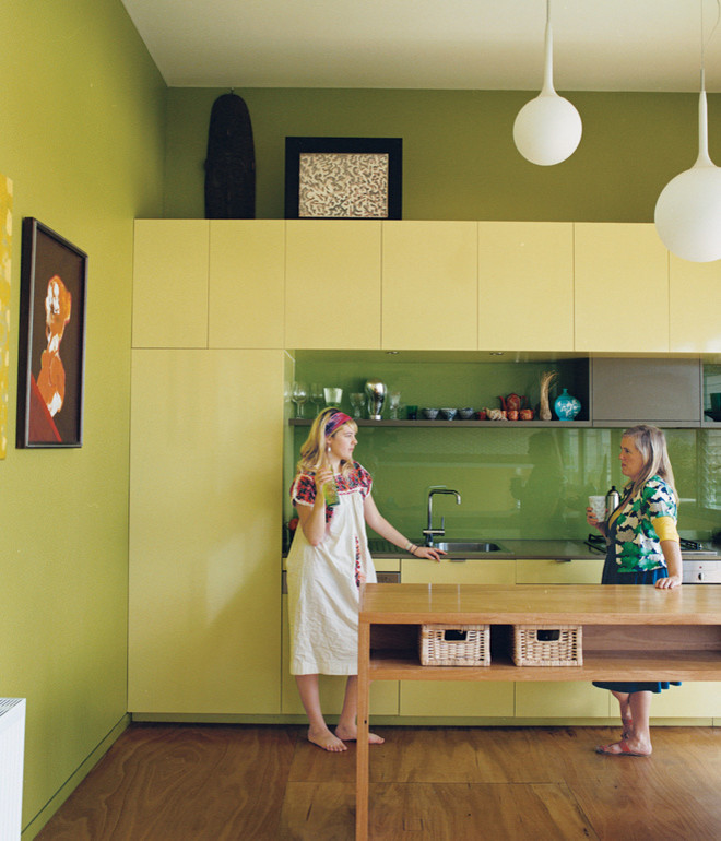 Photo of a medium sized contemporary galley kitchen/diner in Melbourne with a single-bowl sink, flat-panel cabinets, green cabinets, wood worktops, green splashback, glass sheet splashback, integrated appliances, plywood flooring and an island.