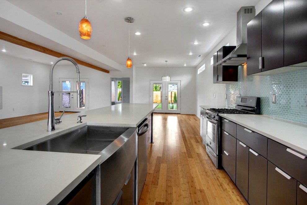Large minimalist galley medium tone wood floor eat-in kitchen photo in Seattle with a farmhouse sink, flat-panel cabinets, dark wood cabinets, blue backsplash, mosaic tile backsplash, stainless steel appliances and a peninsula