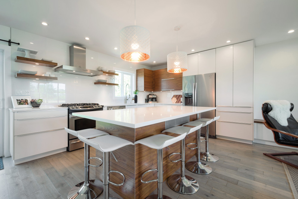 Inspiration for a contemporary l-shaped open plan kitchen in Detroit with a submerged sink, flat-panel cabinets, white cabinets, white splashback, stainless steel appliances, medium hardwood flooring, an island, brown floors and white worktops.