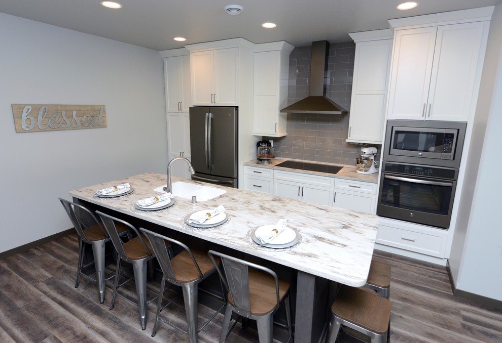 Photo of a small rural galley kitchen/diner in Other with a submerged sink, shaker cabinets, white cabinets, composite countertops, grey splashback, ceramic splashback, stainless steel appliances, laminate floors, an island, brown floors and beige worktops.