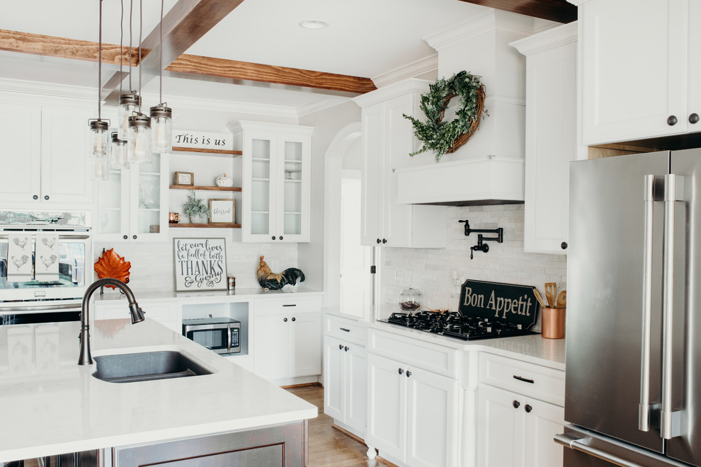 Photo of a large rural l-shaped kitchen/diner in Charlotte with a submerged sink, recessed-panel cabinets, white cabinets, engineered stone countertops, white splashback, stone tiled splashback, stainless steel appliances, medium hardwood flooring, an island, brown floors and white worktops.