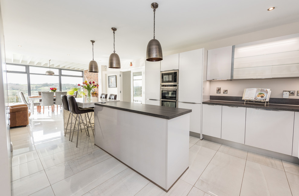 This is an example of a modern kitchen/diner in Other with flat-panel cabinets, white cabinets, marble worktops, stainless steel appliances, porcelain flooring and an island.