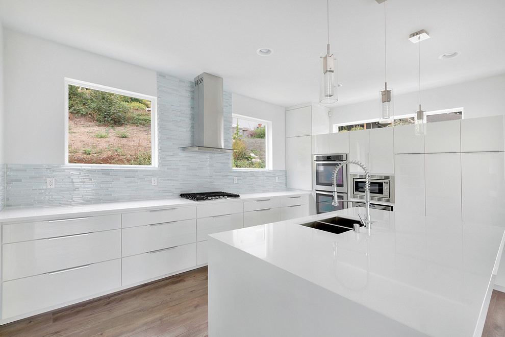 Example of a mid-sized minimalist u-shaped light wood floor kitchen pantry design in Seattle with a double-bowl sink, flat-panel cabinets, white cabinets, quartz countertops, gray backsplash, glass tile backsplash, stainless steel appliances and an island