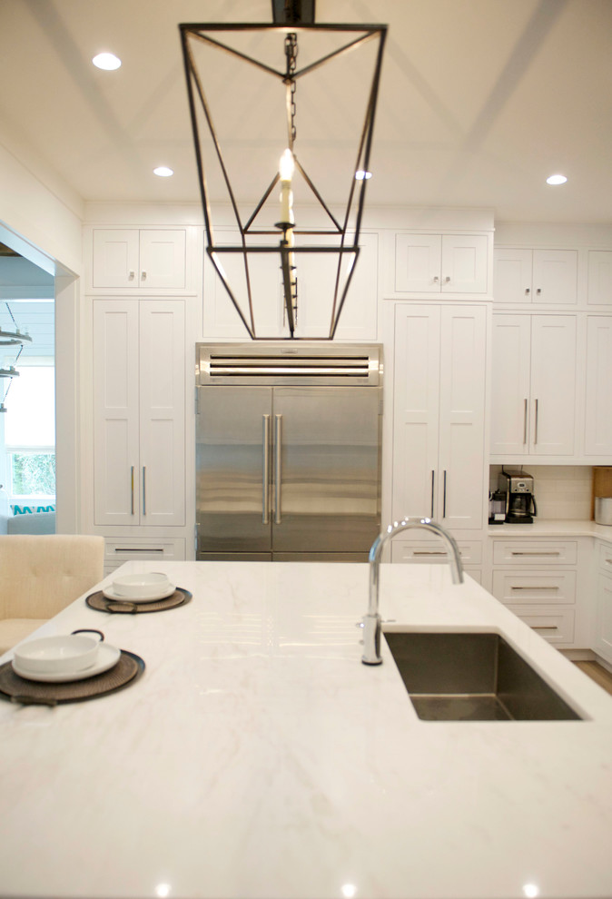 Bild på ett mellanstort funkis kök, med en undermonterad diskho, skåp i shakerstil, vita skåp, marmorbänkskiva, vitt stänkskydd, stänkskydd i tunnelbanekakel, rostfria vitvaror, ljust trägolv och en köksö
