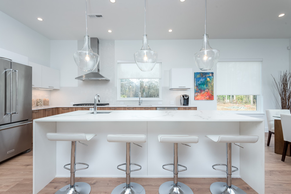 Inspiration for a medium sized contemporary l-shaped kitchen/diner in Charlotte with a submerged sink, flat-panel cabinets, white cabinets, engineered stone countertops, white splashback, porcelain splashback, stainless steel appliances, laminate floors, an island and brown floors.