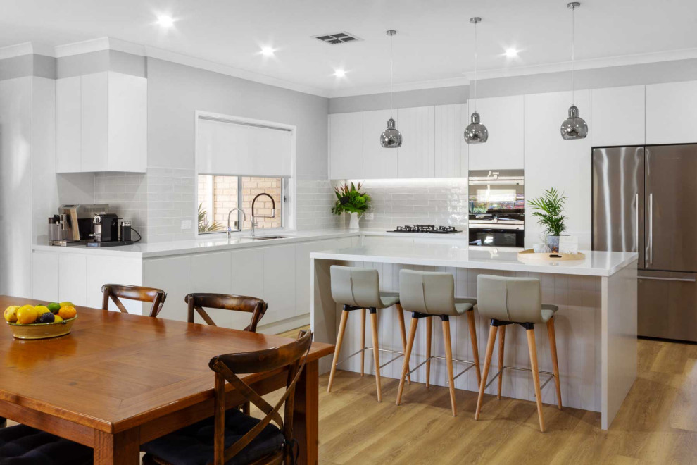 Example of a mid-sized trendy l-shaped vinyl floor and brown floor open concept kitchen design in Sydney with a double-bowl sink, flat-panel cabinets, white cabinets, quartz countertops, gray backsplash, ceramic backsplash, black appliances, an island and white countertops