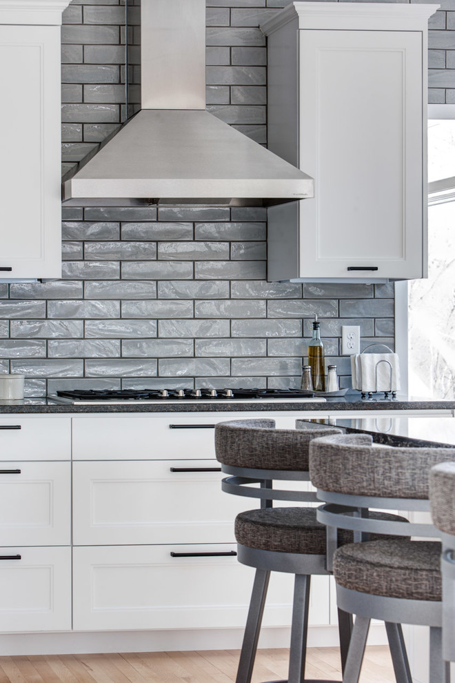 Photo of a large modern l-shaped kitchen/diner in Minneapolis with an island, a submerged sink, recessed-panel cabinets, white cabinets, granite worktops, grey splashback, ceramic splashback, stainless steel appliances and light hardwood flooring.