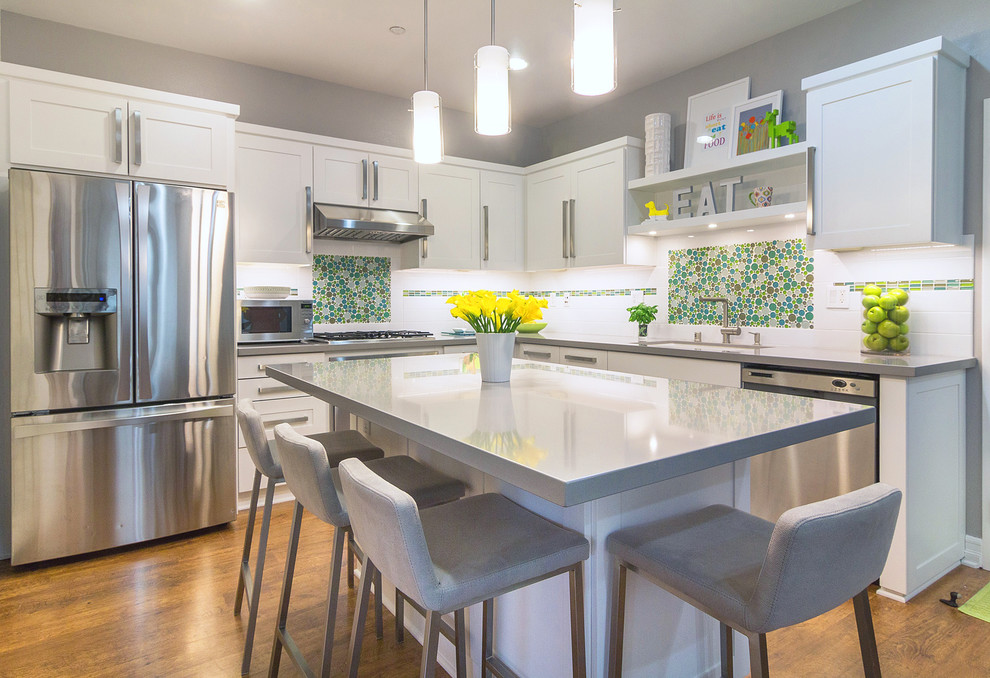 Example of a mid-sized minimalist l-shaped eat-in kitchen design in Orange County with a single-bowl sink, shaker cabinets, white cabinets, quartz countertops, white backsplash, glass tile backsplash, stainless steel appliances and an island