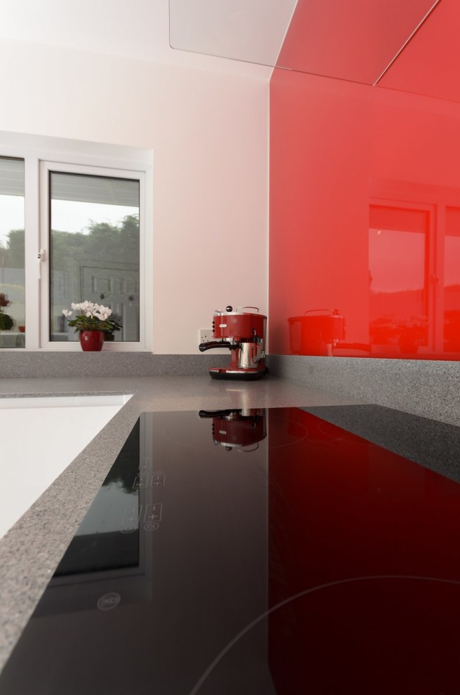 Mittelgroße Moderne Wohnküche ohne Insel in L-Form mit flächenbündigen Schrankfronten, weißen Schränken, Küchenrückwand in Rot und grauer Arbeitsplatte in Sussex