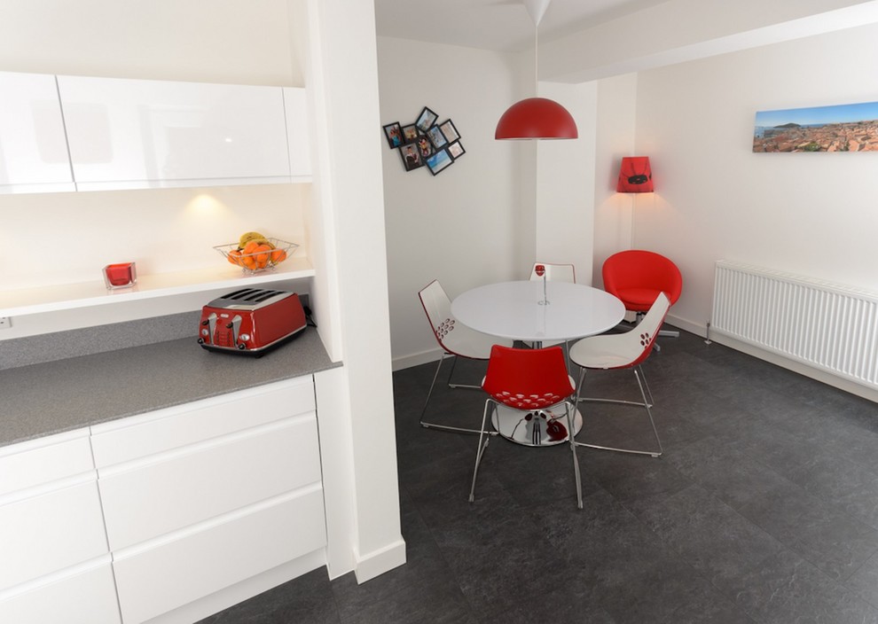 Mittelgroße Moderne Wohnküche ohne Insel in L-Form mit flächenbündigen Schrankfronten, weißen Schränken, Küchenrückwand in Rot und grauer Arbeitsplatte in Sussex
