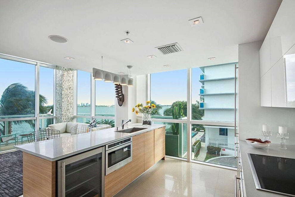 Medium sized modern kitchen in Miami with flat-panel cabinets, light wood cabinets, terrazzo worktops, mirror splashback, stainless steel appliances, an island, white worktops and white floors.