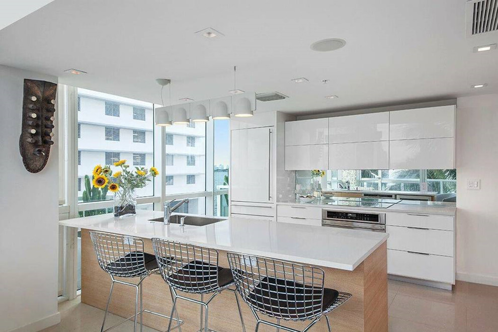 Mittelgroße Moderne Küche mit flächenbündigen Schrankfronten, hellen Holzschränken, Arbeitsplatte aus Terrazzo, Rückwand aus Spiegelfliesen, Küchengeräten aus Edelstahl, Kücheninsel, weißer Arbeitsplatte und weißem Boden in Miami