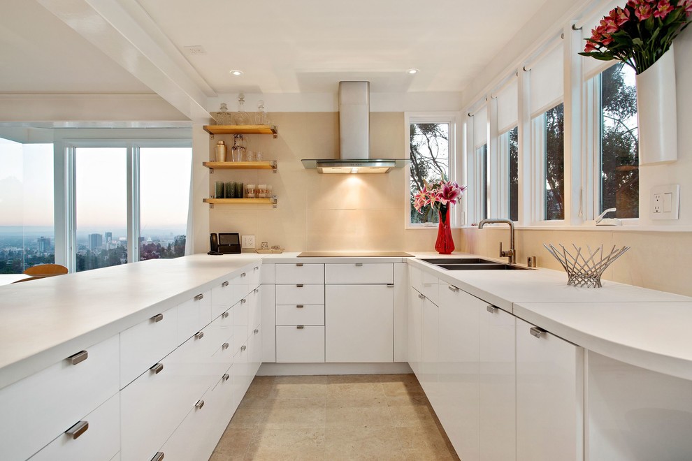 Inspiration for a large contemporary u-shaped kitchen in Los Angeles with a double-bowl sink, flat-panel cabinets, white cabinets, beige splashback, a breakfast bar, composite countertops, porcelain splashback, stainless steel appliances and beige floors.