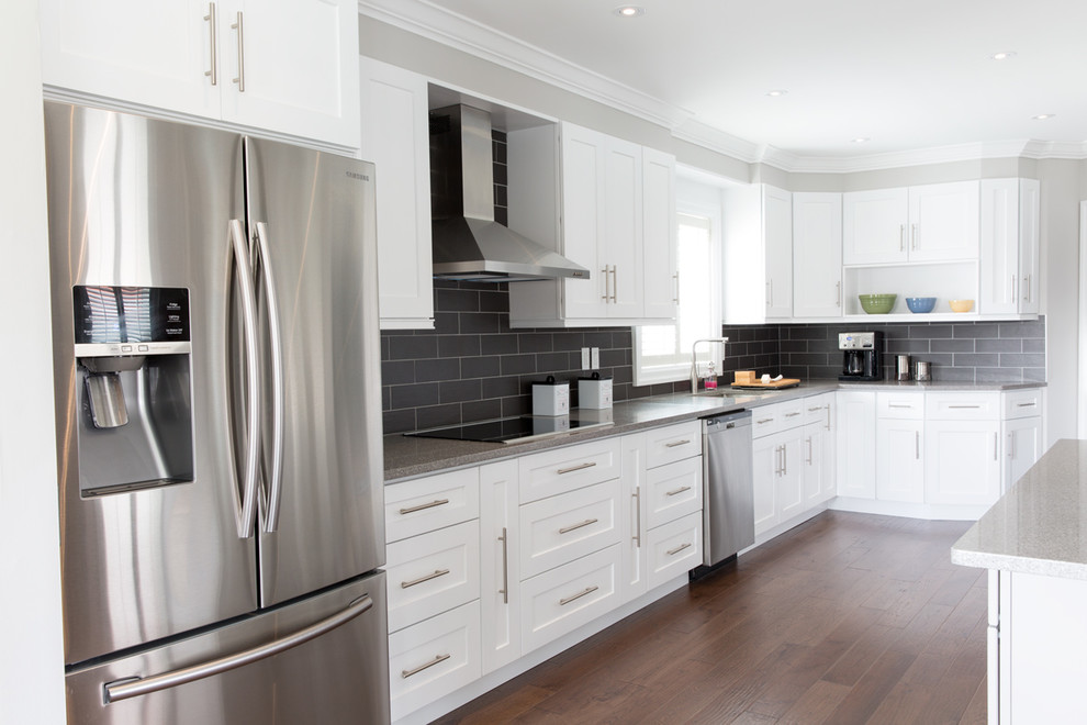 This is an example of a medium sized modern l-shaped enclosed kitchen in Toronto with a submerged sink, shaker cabinets, white cabinets, engineered stone countertops, black splashback, ceramic splashback, stainless steel appliances, medium hardwood flooring and a breakfast bar.