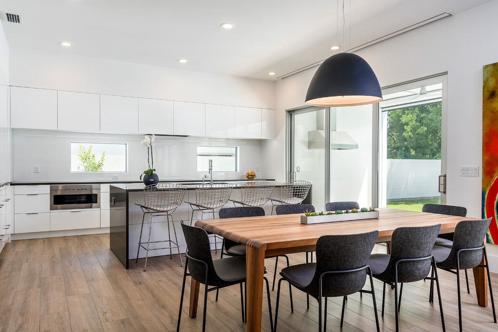Photo of a contemporary kitchen/diner in Orlando with flat-panel cabinets, white cabinets, white splashback, stainless steel appliances, medium hardwood flooring and an island.