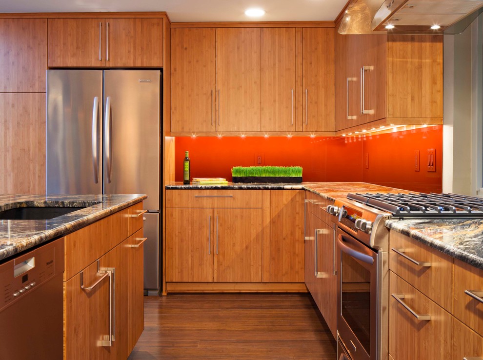 Modern inredning av ett stort kök, med en undermonterad diskho, släta luckor, skåp i mellenmörkt trä, granitbänkskiva, orange stänkskydd, bambugolv och en köksö