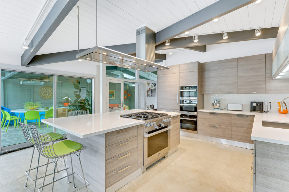 Cette photo montre une cuisine américaine encastrable moderne en L et bois clair avec un évier encastré, un placard à porte plane, îlot et un plan de travail blanc.