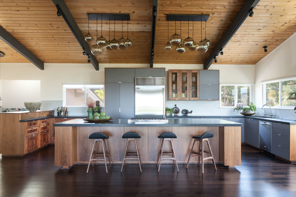 Imagen de cocinas en U actual con fregadero bajoencimera, armarios con paneles lisos, puertas de armario grises, electrodomésticos de acero inoxidable, suelo de madera oscura, una isla y encimera de granito