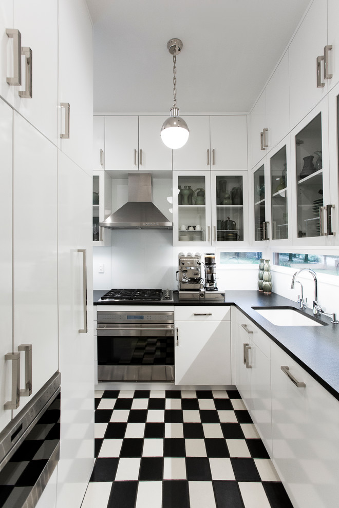 Bild på ett litet funkis kök, med en undermonterad diskho, släta luckor, vita skåp, granitbänkskiva, vitt stänkskydd, glaspanel som stänkskydd, rostfria vitvaror och klinkergolv i keramik